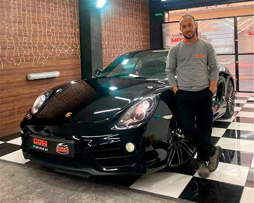 Técnico de detailing junto a un coche deportivo negro con acabado brillante en el taller
