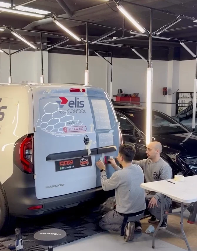 Dos técnicos aplicando vinilo y rotulación en la parte trasera de una furgoneta de empresa